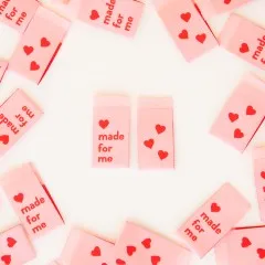Mehrere rosa Weblabels mit Schriftzug "Made for Me" und Herz-Rückseite im Kreis um zwei zentrale Labels angeordnet.
