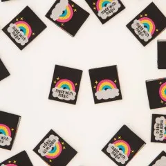 Schwarze Weblabels mit goldglänzendem Regenbogen, Wolke und Schriftzug „made with magic" verstreut auf hellem Untergrund.