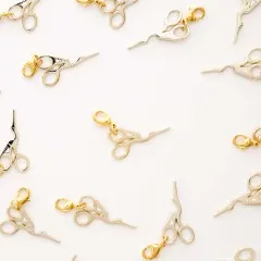 Mehrere Storchenscheren-Zipper-Charms locker verstreut auf hellem Untergrund.