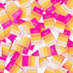 Dichte Nahaufnahme vieler verstreuter gestreifter Weblabels mit goldener „Cut Sew Press Repeat"-Schrift.