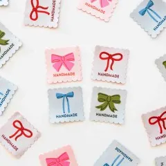 Mehrere Bows-Handmade-Weblabels in verschiedenen Farben locker verstreut auf weißem Untergrund.