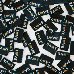 Dichte Nahaufnahme vieler verstreuter schwarzer „LOVE"-Weblabels mit Regenbogenherz.