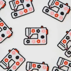 Nahaufnahme mehrerer Nähmaschinen-Patches mit rosa, roten und schwarzen Blüten, dicht verstreut.