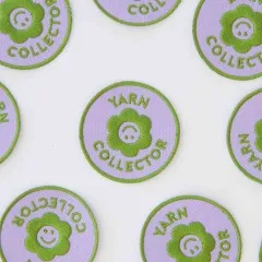 Mehrere Yarn-Collector-Patches verstreut, mit wechselnder Ausrichtung von Blüten-Smiley und Schriftzug.