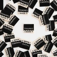 Mehrere schwarze Sarah-Hearts-Weblabels „Thanks I Made It" mit weißem Siebdruck, ein Label mittig freigestellt.