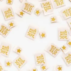 Mehrere cremefarbene Sarah-Hearts-Weblabels „Made with Joy" mit goldenem Stern-Aufdruck, ein Label mittig freigestellt neben einem goldenen Stern.