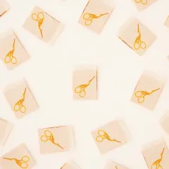 Naturfarbene Weblabels mit goldfarbenem Storchenscheren-Motiv verstreut auf hellem Untergrund.