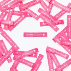 Mehrere pinke Sarah Hearts Weblabels „You are Beautiful" kreuz und quer verstreut um ein einzelnes Label angeordnet.