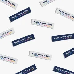 Zahlreiche „Made With Love & Swear Words"-Labels in Marineblau und Creme als Flatlay-Musteraufnahme locker verstreut.