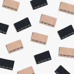 Zahlreiche „You Can't Buy This"-Labels in Schwarz und Kamel als Flatlay-Musteraufnahme locker verstreut.