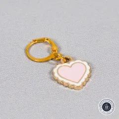 Nahaufnahme des rosa Herz-Anhängers mit weißem Rüschenrand auf grauem Stoff.