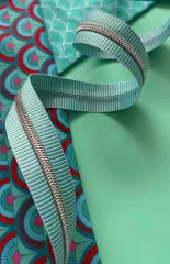 Nähere Ansicht des geschwungenen Teal-Stripe-Reißverschlussbands auf den gemusterten Patchworkstoffen.