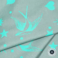 Nahaufnahme des diagonal gefalteten Stoffs „Neon Fairy Flakes“ in Spirit, Schwalben- und Sternmotive in Türkis gut erkennbar.