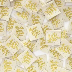 Viele Sarah Hearts Weblabels „Made for you" in Metallic-Gold dicht verstreut, Nahaufnahme.