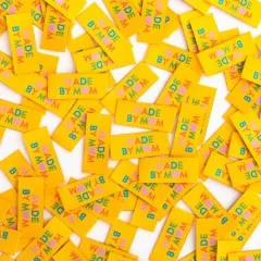 Dicht verstreute gelbe Weblabels "Made by Mom" mit buntem Herz-Schriftzug in Nahaufnahme.