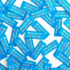 Dicht verstreute türkisblaue Weblabels mit dem Schriftzug "Made by Grandma" in Nahaufnahme.
