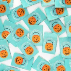 Dicht verstreute mintgrüne Weblabels mit orangefarbenem Kürbiseimer-Motiv in Nahaufnahme.