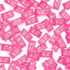Dicht verstreute pinke Weblabels mit dem Schriftzug "To: You, Herz: Me" in Nahaufnahme.