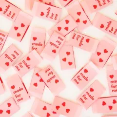 Dicht verstreute rosa Weblabels mit Schriftzug "Made for Me" und Herzen in Nahaufnahme.