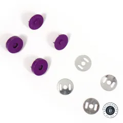 Nahaufnahme der violetten Druckknopf-Hälften mit sichtbaren Metallstiften auf der Rückseite, daneben vier gelochte Unterlegscheiben.
