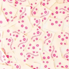 Viele cremefarbene Sarah Hearts Weblabels mit pinken Blüten dicht verstreut, Nahaufnahme.