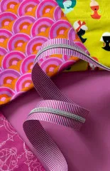 Nahaufnahme des pink-lila gestreiften Reißverschlussbandes auf farbenfrohen gemusterten Baumwollstoffen in Orange, Magenta und Gelb.