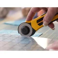 Hand führt gelben OLFA Rollschneider mit 45 mm Klinge entlang eines Patchwork-Lineals über Stoff