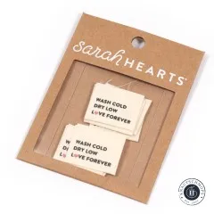 Sarah Hearts Bio-Baumwoll-Weblabel „Wash Cold, Dry Low, Love Forever“ auf der Original-Verpackungskarte.