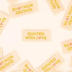 Sarah Hearts Weblabels „Quilted with Love" in Gold locker verteilt auf weißem Untergrund