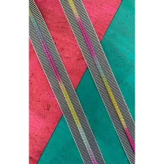 Drei parallel ausgelegte Stränge des schwarz-weiß gestreiften Bandes mit Regenbogen-Zahnreihe in Lila, Magenta, Gold und Türkis auf pink-türkisfarbenem Korkuntergrund.