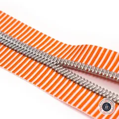 Nahaufnahme des orange-weiß gestreiften Bandes mit silberfarbener Zahnreihe auf weißem Hintergrund, zwei Stränge diagonal überkreuzt.