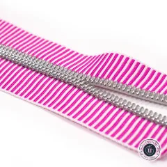 Extreme Nahaufnahme des pink-lila gestreiften Bandes mit silberfarbener Zahnreihe auf weißem Hintergrund, diagonal ausgerichtet.