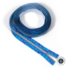 Aufgerolltes Reißverschluss-Endlosband mit blauen Pebble-Punkten auf violettem Grund und silberfarbener Verzahnung, freigestellt auf Weiß.