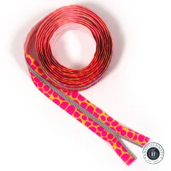 Aufgerolltes Reißverschluss-Endlosband mit pinkfarbenen Pebble-Punkten auf orangegelbem Grund, silberfarbene Zähne, freigestellt auf Weiß.