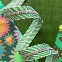 Nahaufnahme des Reißverschlussbandes auf Korkuntergrund mit Blumen- und Krokodilmuster im Hintergrund.