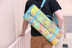 Person trägt den gefalteten Ruler Wrap in gelb-türkisem Blumenstoff über der Schulter.