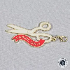 Schere- und Knopf-Anhänger nebeneinander auf grauem Stoff.
