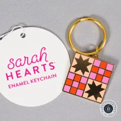Sarah Hearts x Then Came June Emaille-Schlüsselanhänger im Quilt-Sternmuster, neben der Anhängekarte auf grauem Stoff.