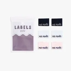 Alle sechs Labels 'me made' in Schwarz, Weiß und Rosa neben der Verpackung.