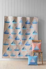 Patchwork-Quilt mit Segelboot-Muster aus der Summer-Kollektion, an der Wand aufgehängt, mit Kissen auf Stuhl.