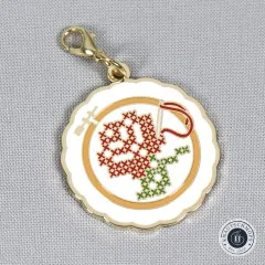 Nahaufnahme des Anhängers in Form eines Stickrahmens mit rot-grünem Kreuzstich-Rosenmotiv.