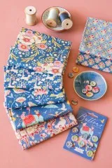 Stoffstapel der Jubilee-Kollektion Blue dekorativ arrangiert mit Nähgarn und Knöpfen