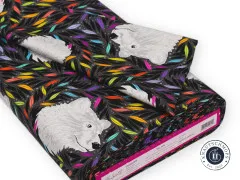 Gefalteter Stoffballen mit Bärenkopf-Motiv „Just Bearly" und bunten Blättern auf dunklem Grund.