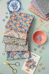 Die blauen Wallflower-Stoffe in einem dekorativen Flatlay mit Porzellanteller, Knöpfen und Schere.