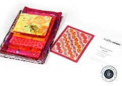 Gestapelte Baumwollstoffe in Pink, Orange und Rot neben gedruckter Anleitung zum Watercourse Quilt