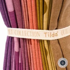 Nahaufnahme der gefalteten Stoffkanten in Violett, Beere, Orange und Senfgelb mit dem Baumwollband „Tilda Quilt Collection".