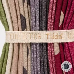 Nahaufnahme der gefalteten Stoffkanten in Grün, Beige, Grau und Beere mit dem Baumwollband „Tilda Quilt Collection".