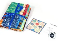 Gebündelte Stoffe des Quilt Kits mit blauem Satinband neben bebilderter Anleitung Trellis Twist
