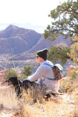Wanderer mit Hund trägt die Switchback-Tasche als Rucksack vor einer Berglandschaft.