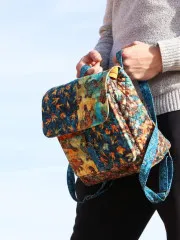 Nahaufnahme der Switchback-Tasche in blau-goldenem Safari-Batik-Stoff, in der Hand getragen.